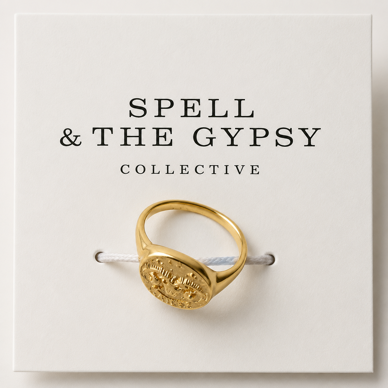 A gold signet ring with an engraved circular face, displayed on a white card printed with the brand name 'SPELL & THE GYPSY COLLECTIVE'.