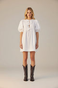 Person wearing a white dress and black cowboy boots on a white background