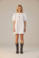 Person wearing a white dress and black cowboy boots on a white background