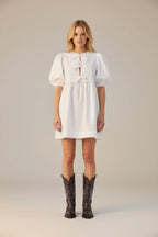 Person wearing a white dress and black cowboy boots on a white background