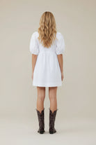 Person wearing a white dress and black cowboy boots on a white background