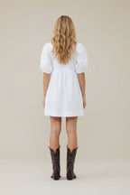 Person wearing a white dress and black cowboy boots on a white background