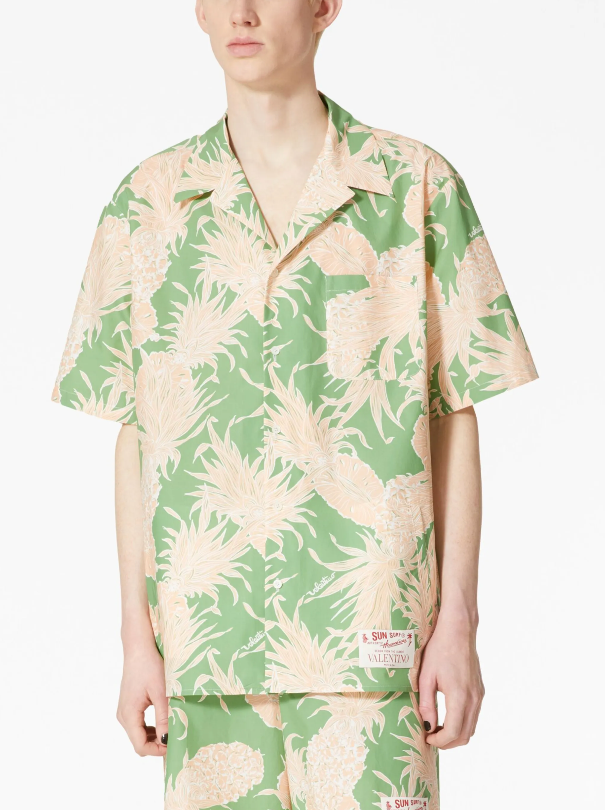 A male model wearing a green and beige pineapple print cotton Hawaiian bowling shirt with a Cuban collar.
