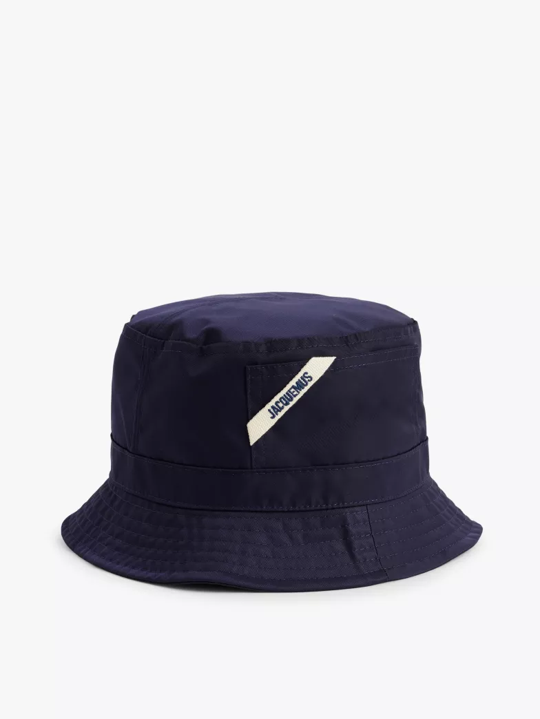 A navy blue bucket hat with a wide brim and a white brand tag embroidered on the front.