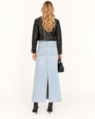 Agolde Della Denim High Rise Midi Skirt A woman shown from the back wearing a light blue wide-leg denim skirt, a black leather cropped jacket, and black ankle boots, holding a small black handbag against a plain white studio background.