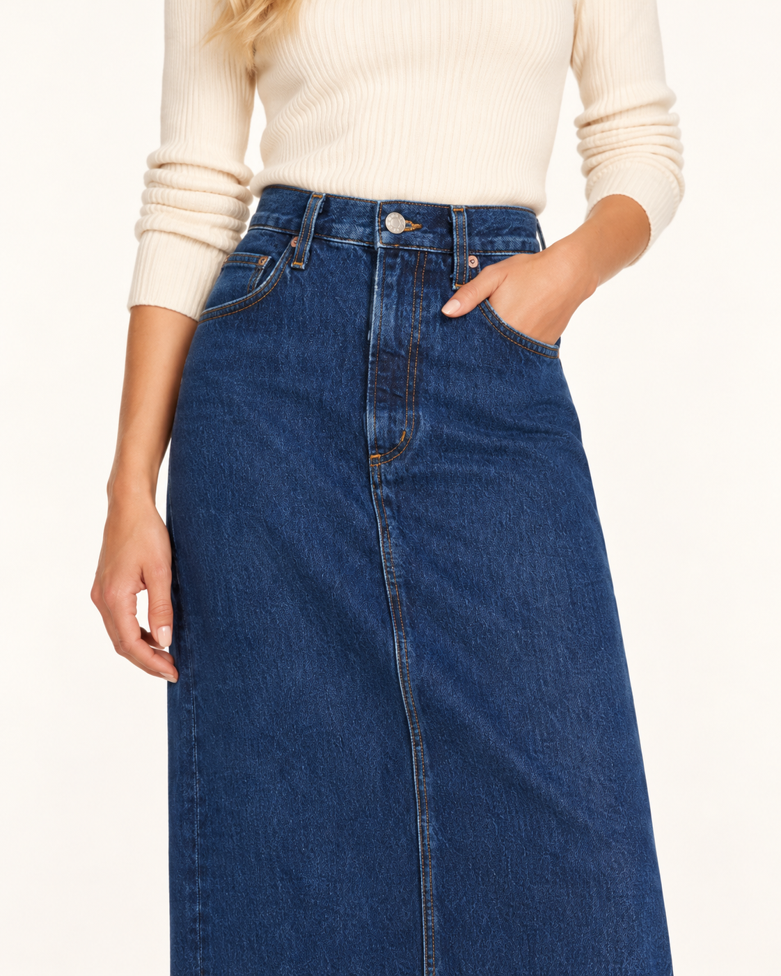 Agolde Hilla Denim Maxi Skirt A model wearing a high-waisted, mid-length blue denim skirt with a front zipper and side pockets, paired with a cream ribbed knit sweater, against a plain white background.