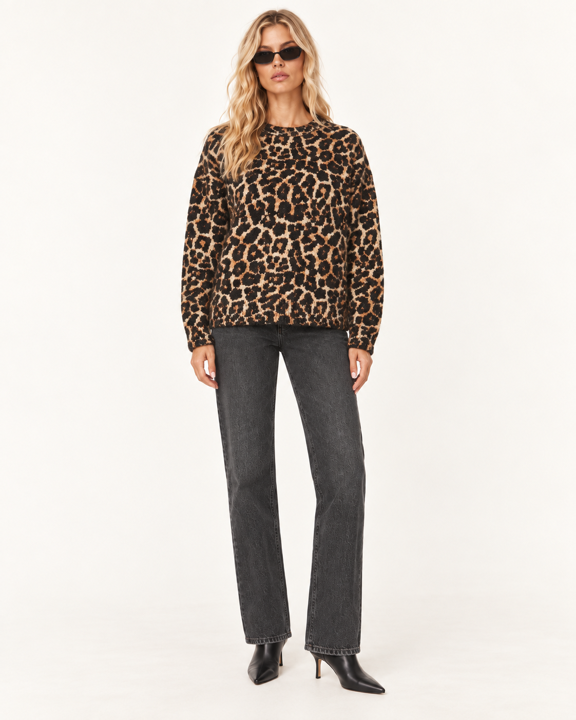 Anine Bing Leopard Print Sydney Brushed Wool Jumper A woman modeling a leopard-print long-sleeve top with dark gray jeans and black pointed-toe heels, standing against a plain white studio background.