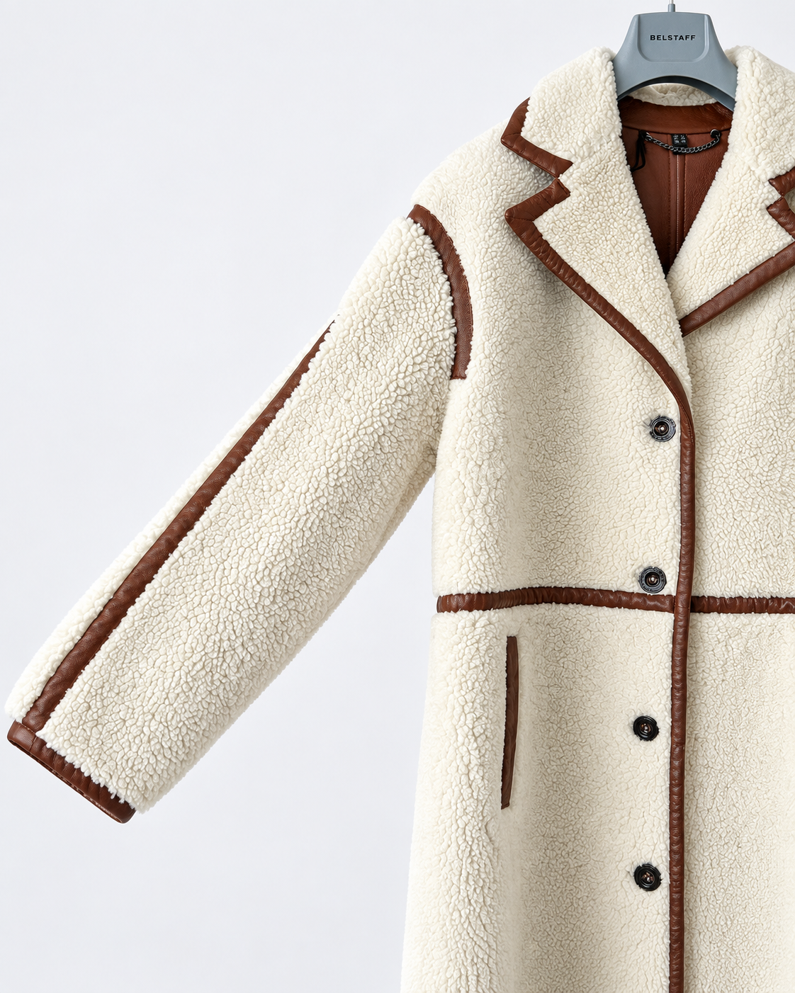 A cream-colored sherpa fleece coat with brown faux-leather trim and buttons, hanging on a gray hanger against a light gray background.