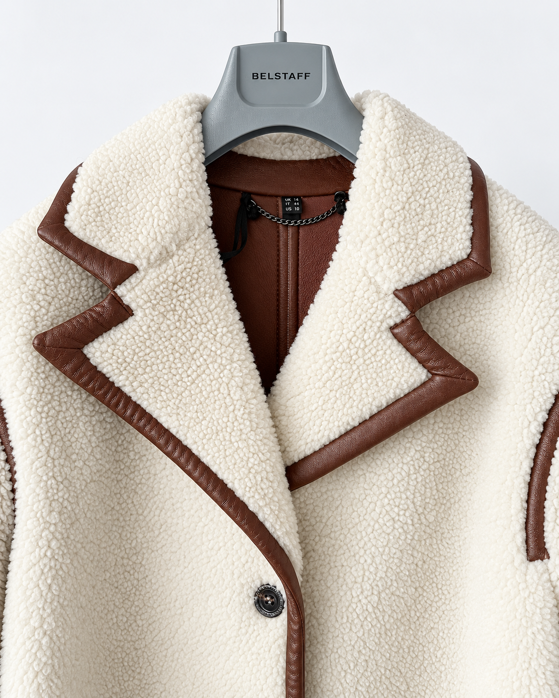 Belstaff Airstream Women’s Shearling Coat A close-up of a cream-colored sherpa fleece jacket with brown leather trim, hanging on a gray BELSTAFF hanger against a light gray background.