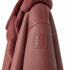 Belstaff Cedar Shearling Leather Jacket Close-up of a brown faux-leather jacket with a plush brown sherpa lining and a square embossed BELSTAFF logo patch on the upper sleeve, set against a plain white background.