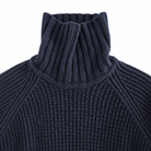 Close-up of a dark navy ribbed knit turtleneck sweater showing the high collar and textured knit pattern against a plain white background.