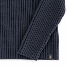 Close-up of a navy ribbed knit sweater with a folded sleeve, showing the texture and a small gold embroidered logo patch near the hem.