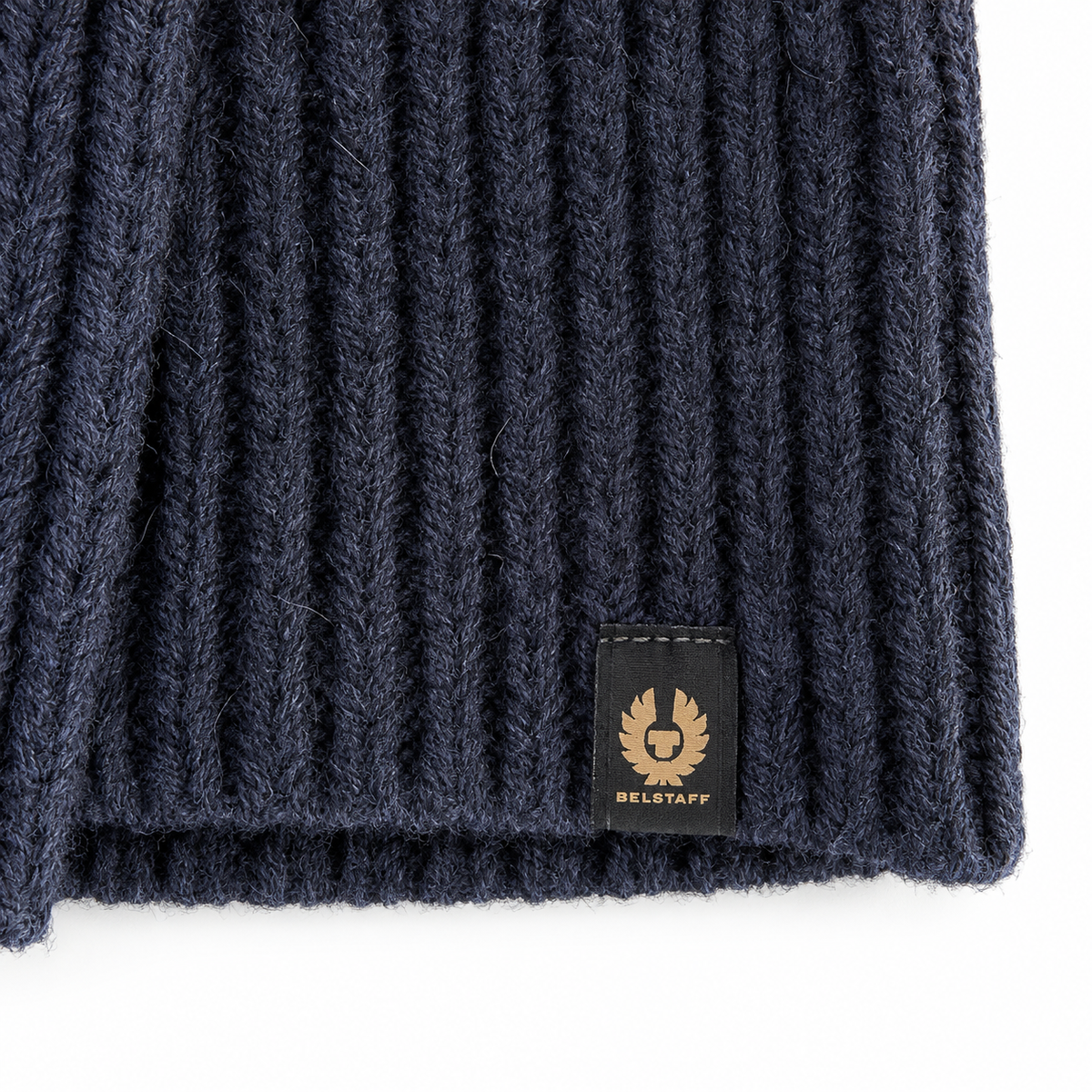 Belstaff Marine Roll Neck Jumper Navy Close-up of a dark navy ribbed knit fabric with a small black BELUGAFF patch featuring a gold logo, set against a plain white background.