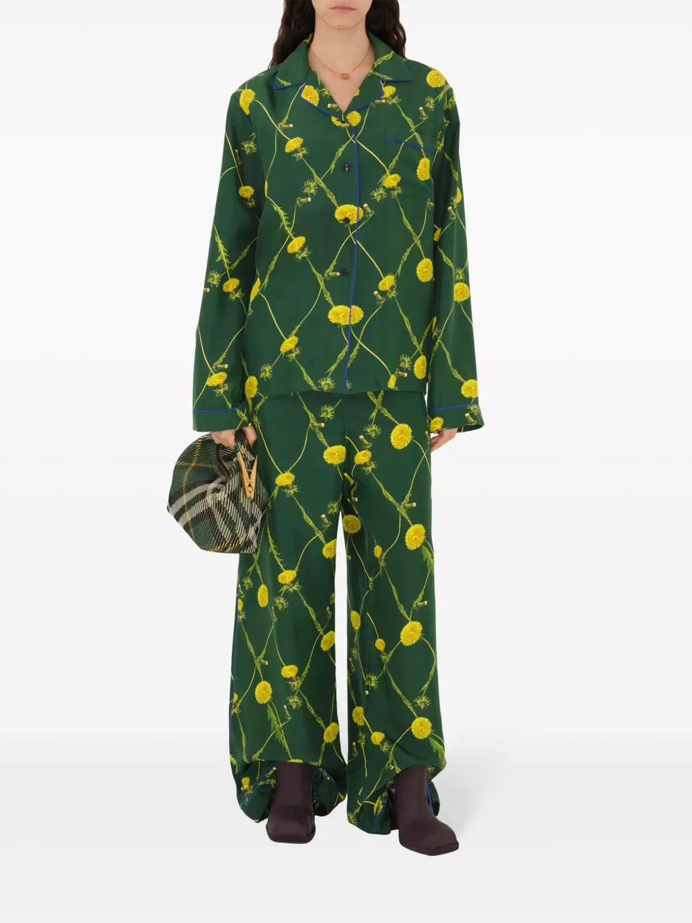 A model wearing a Burberry dandelion print silk pyjama shirt in green and yellow, paired with matching pants, holding a bag and wearing shoes.