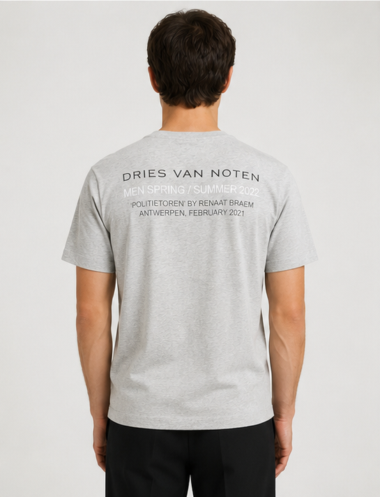 Dries Van Noten Grey Hertz Tower T-Shirt A man viewed from behind wearing a light gray heather t-shirt with black text printed on the back, paired with black pants, against a light gray studio background.