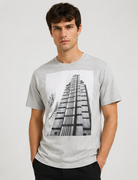 Dries Van Noten Grey Hertz Tower T-Shirt A man wearing a light gray heather crewneck t-shirt with a large black and white graphic print of a modernist building on the front, set against a plain light gray background.