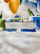 Close-up of a garment label reading 'BORGO DE NOR' with size '12', showing part of a white fabric with a blue, green, and yellow floral print above it.