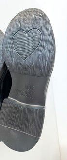 The soles of a pair of black shoes, showing a textured rubber tread with a heart-shaped grip pattern and the brand name 'LOVE MOSCHINO' embossed on the heel.