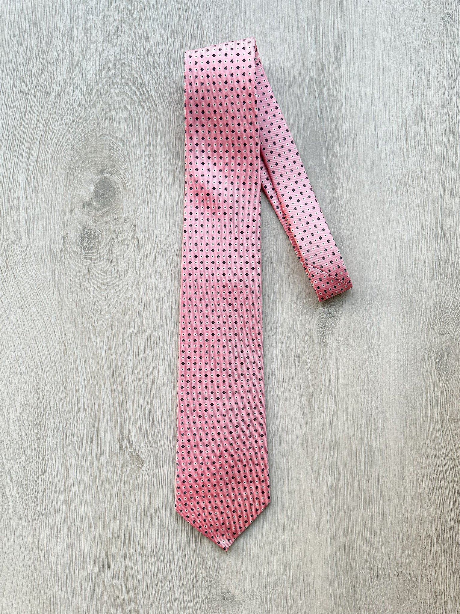 A pink floral patterned tie with a dotted design, laid out on a wooden surface.