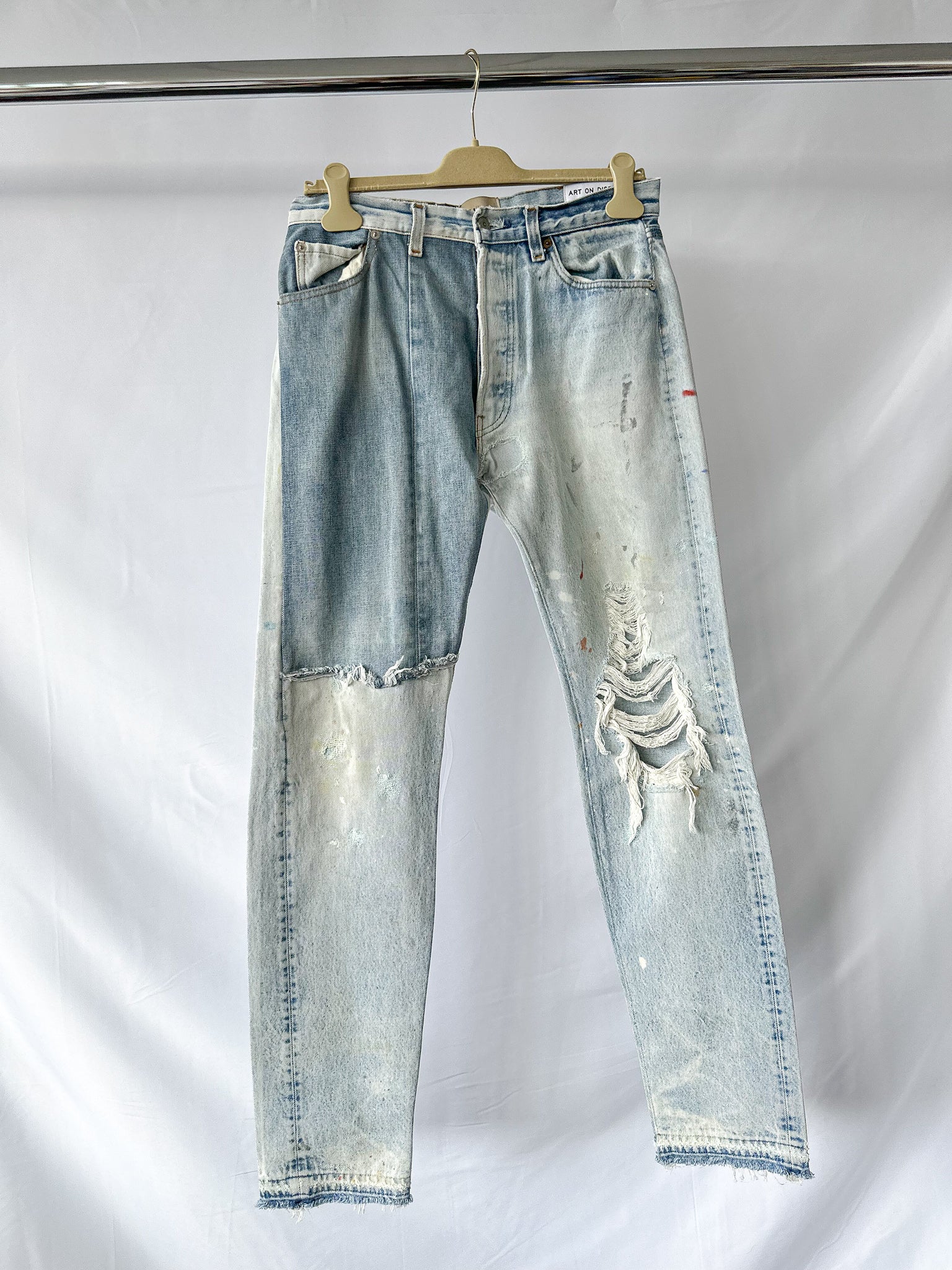 Gallery Dept Ken Levi Distressed blue jeans on a hanger against a white background