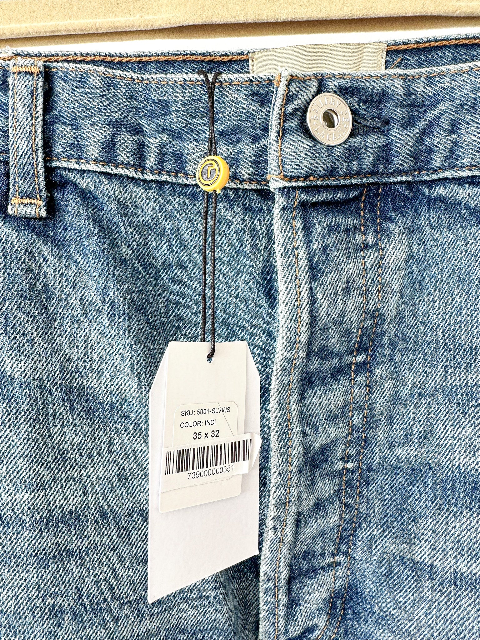 Gallery Dept lose-up of blue jeans with a tag displaying size and brand information.