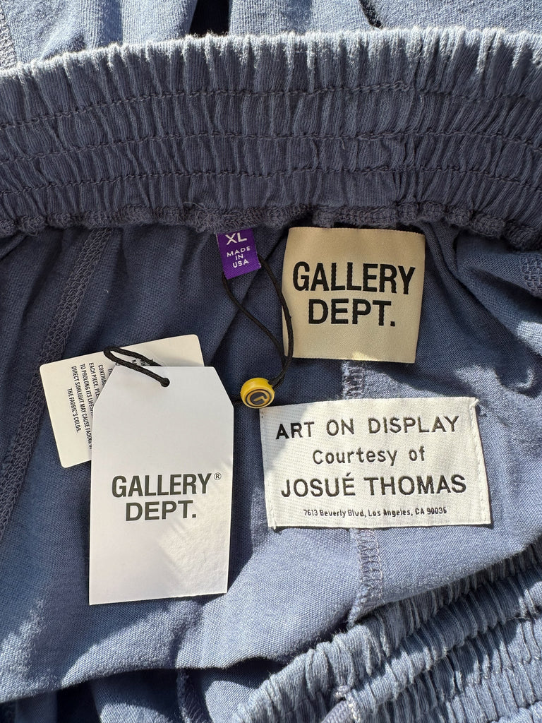 Close-up of clothing tags with 'Gallery Dept.' and 'Josue Thomas' on a textured fabric background.