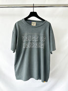 Gray t-shirt with 'HOUSE OF HORRORS' text on a hanger against a white background