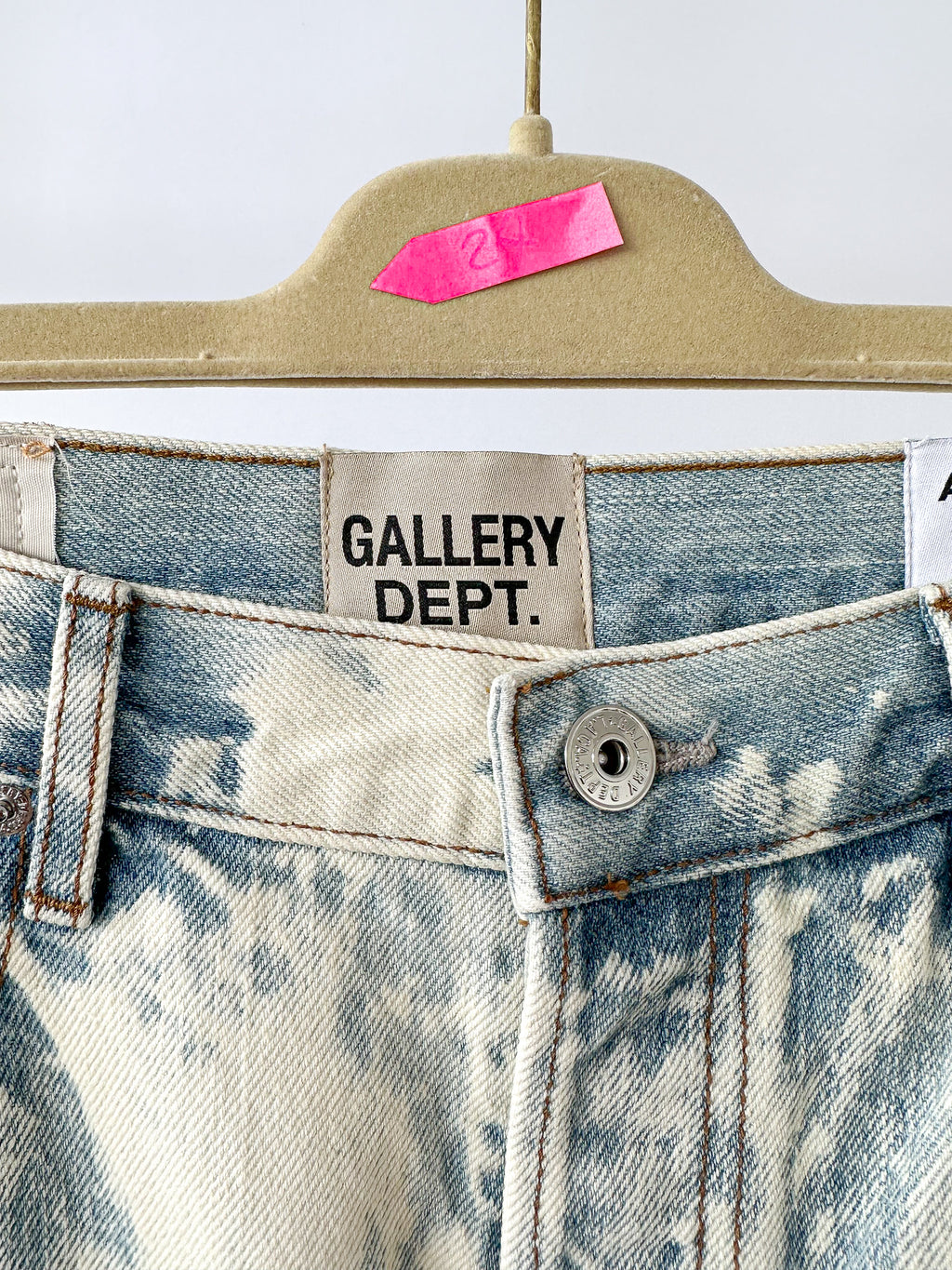 Close-up of a denim garment with 'GALLERY DEPT.' label on a beige hanger.