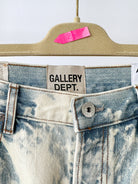 Close-up of a denim garment with 'GALLERY DEPT.' label on a beige hanger.