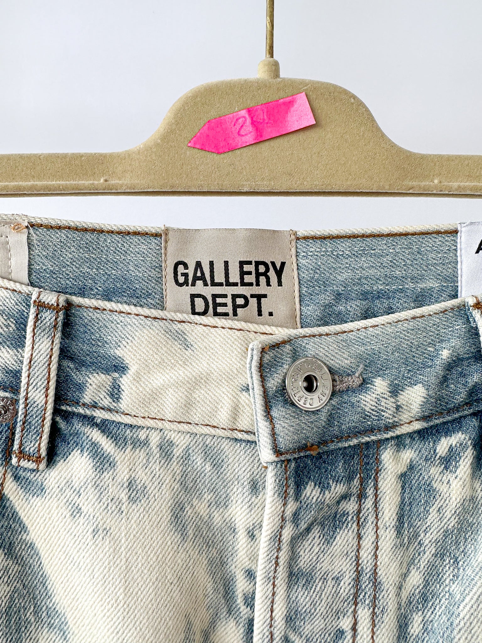Close-up of a denim garment with 'GALLERY DEPT.' label on a beige hanger.