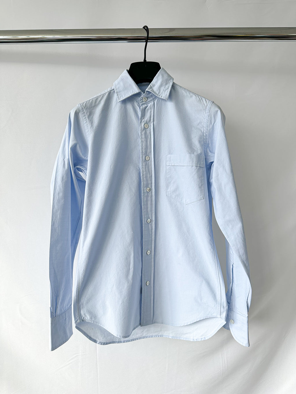 Drake's ight blue button-up shirt on a hanger against a white background