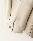 Lemaire Cream Workwear Over Shirt Denim Jacket - Close-up of a light beige or cream-colored canvas jacket sleeve, showing the fabric texture, a buttoned cuff, and neat stitching against a matching light background.