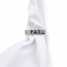 Silver cufflink with 'P de S' engraving on a white shirt sleeve.
