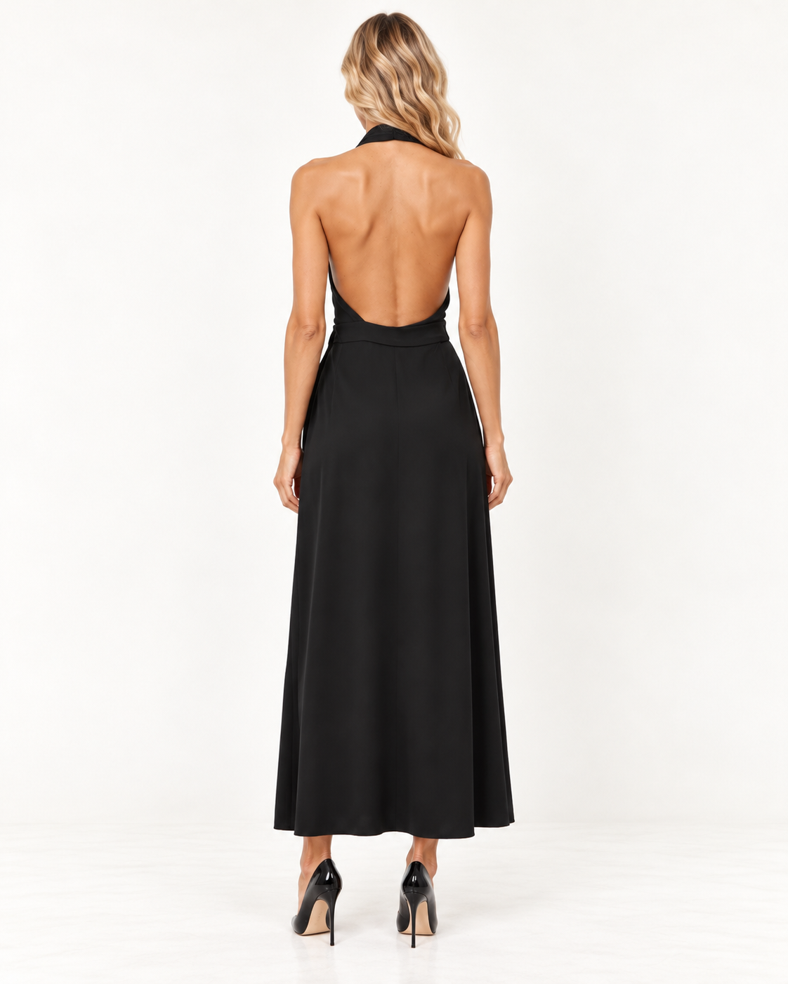 Raey Black Silk Wrap Halterneck Dress A woman viewed from the back wearing a black halter-neck maxi dress with a low open back and black heels, standing against a plain white studio background.