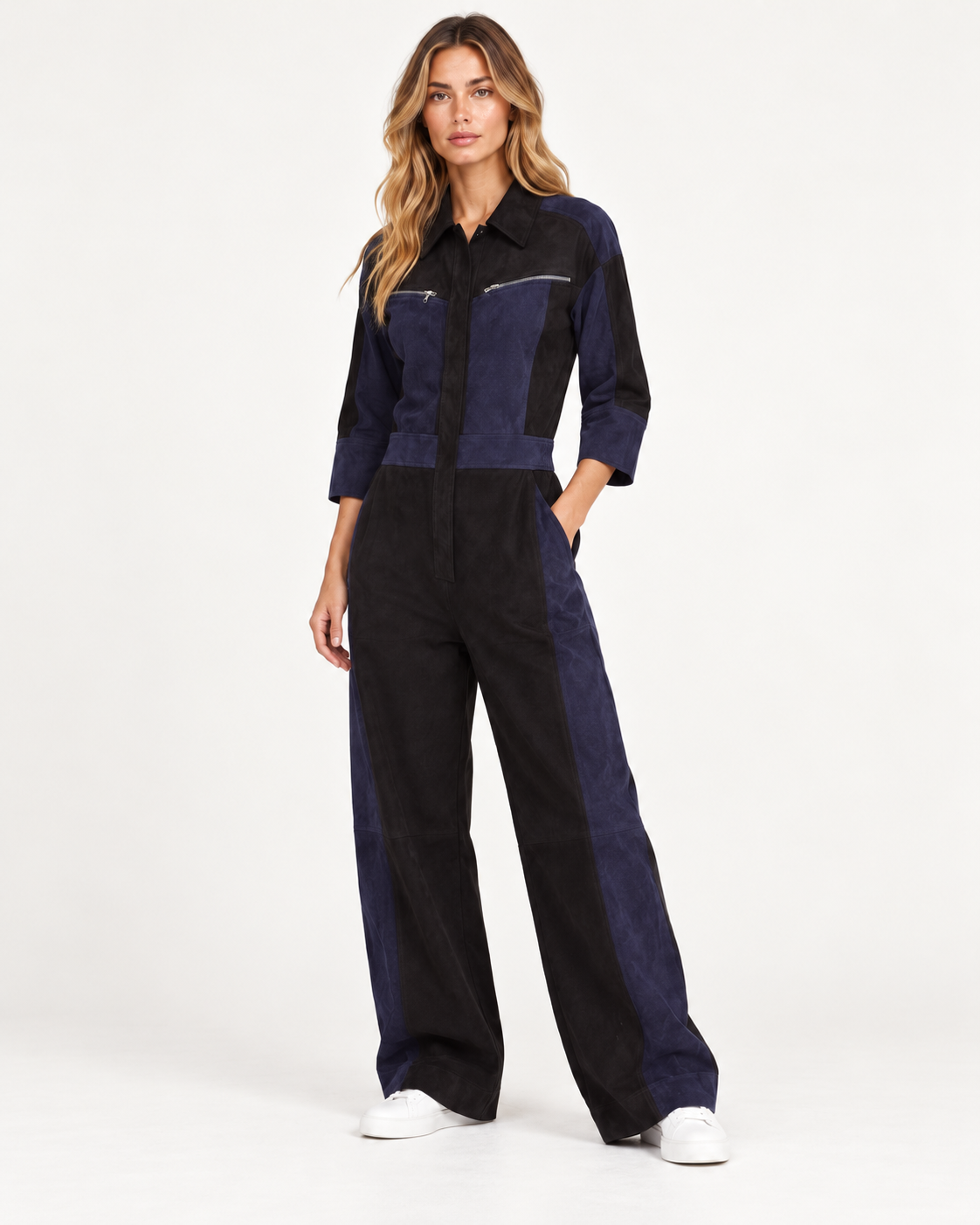 Raey Nappa Suede Leather Patchwork Suede Jumpsuit A woman modeling a color-blocked jumpsuit with a dark navy blue and black color-blocked design, featuring a collared shirt-style top and wide-leg pants, paired with white sneakers against a plain white studio background.