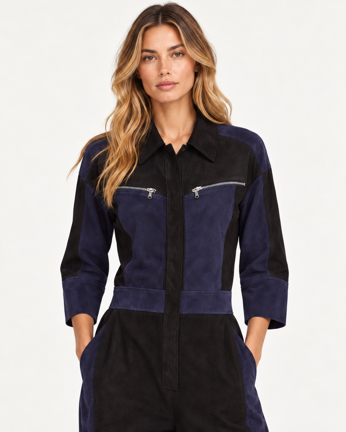 A woman modeling a color-blocked jumpsuit in navy blue and black suede-like fRaey Nappa Suede Leather Patchwork Suede Jumpsuit abric, featuring zippered chest pockets and a button-down front, against a plain white studio background.