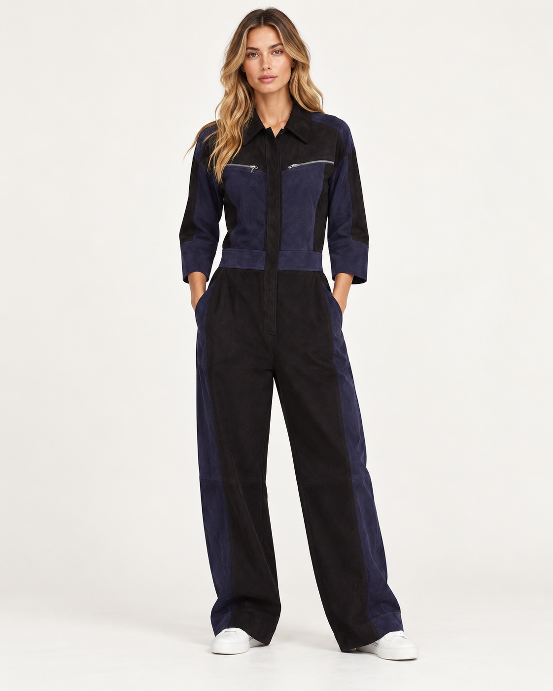 Raey Nappa Suede Leather Patchwork Suede Jumpsuit A woman modeling a color-blocked jumpsuit with a dark navy blue upper section and wide-leg black trousers, standing against a plain white studio background.
