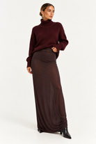 Skims Brown Sheer Modal Long Skirt A woman modeling a dark burgundy ribbed turtleneck sweater and a matching dark brown sheer maxi skirt, paired with black pointed-toe ankle boots, against a plain white studio background.