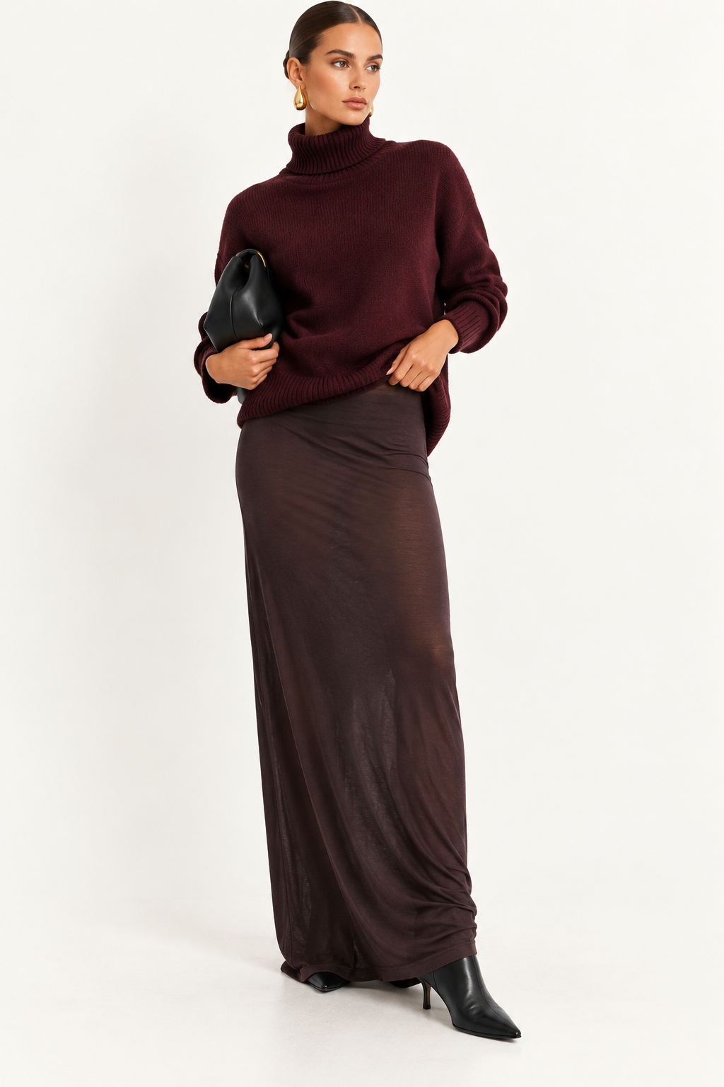 Skims Brown Sheer Modal Long Skirt A woman modeling a dark burgundy turtleneck sweater and a matching dark brown maxi skirt, holding a black clutch against a plain white studio background.