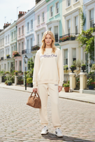 Person wearing a cream  sporty & ricvh 'Wellness Club' sweatshirt and pants, holding a brown bag in Notting Hill 